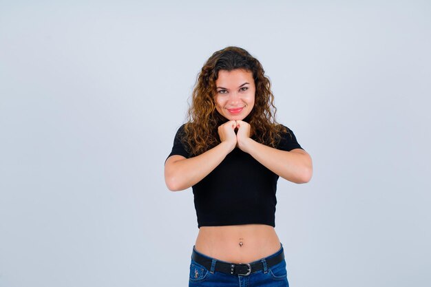 Smiling girl is looking at camera by holding hands together on chest on white background