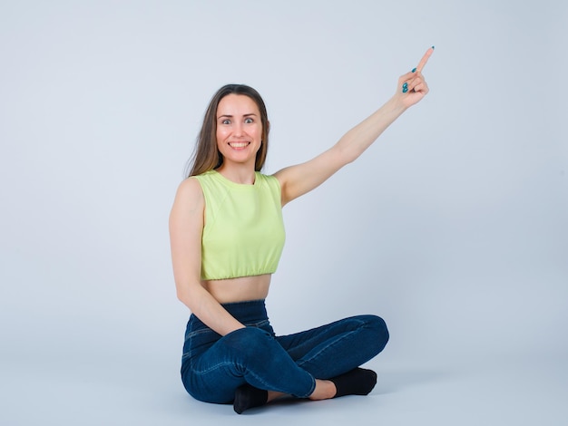 Smiling girl is pointing right up with forefinger by sitting on floor on white background