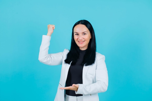 Smiling girl is raising up her fist on blue background