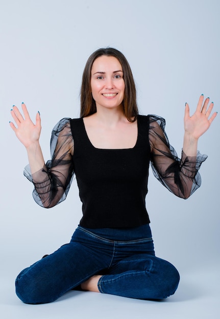 Smiling girl is raising up her handfuls by sitting on floor on white background