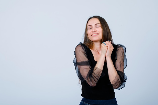 Smiling girl is wishing by holding hands together on white background