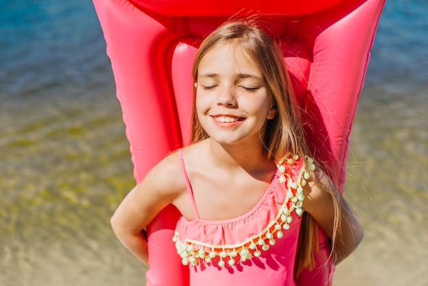 Smiling girl keeping inflatable mattress standing by water