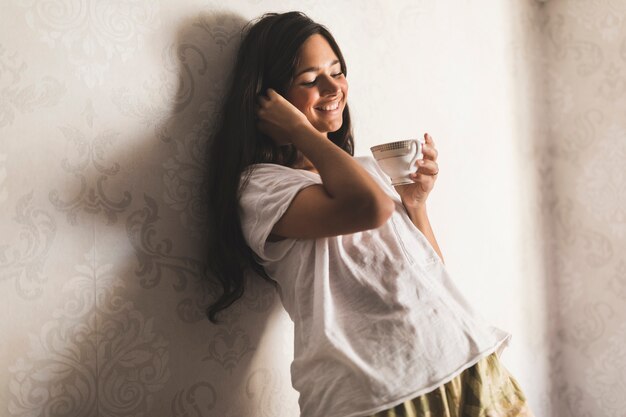 Smiling girl leaning on wallpaper holding coffee cup in hand