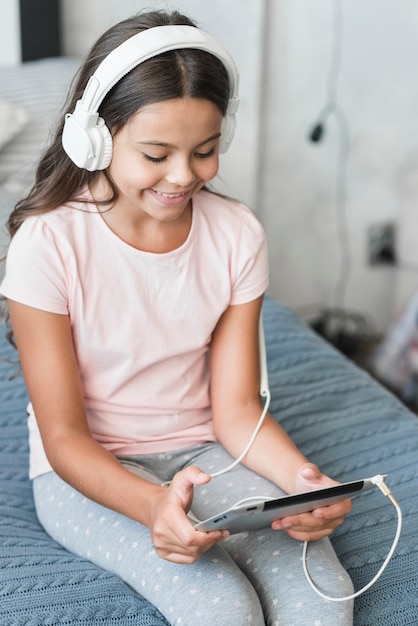 Free Photo smiling girl listening music on headphone through digital tablet