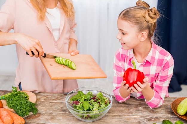 Free photo smiling girl looking at her mother preparing the salad on table