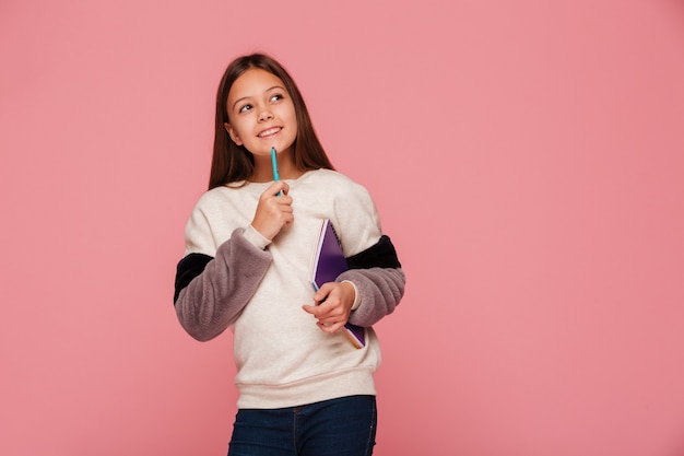 Smiling girl looking up and thinking while holding pencil and books