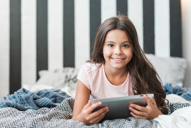 Free photo smiling girl lying on messy bed with digital tablet