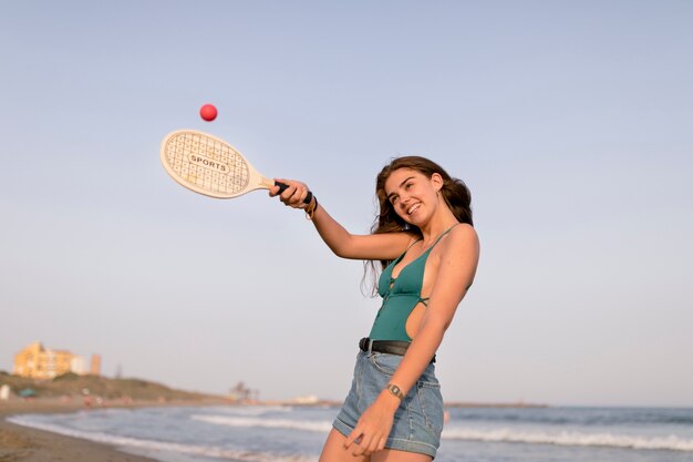 Smiling girl playing with tennis ball and racket at beach