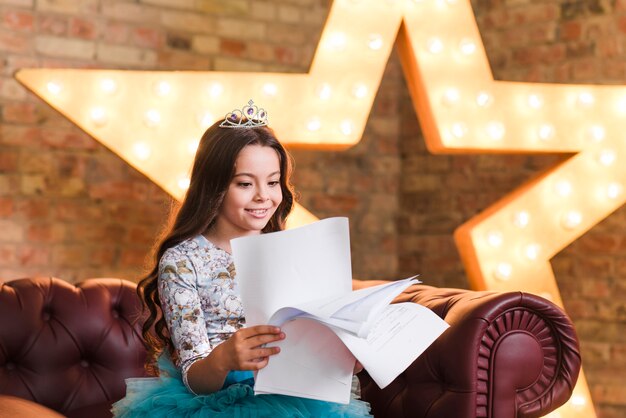 Smiling girl sitting on sofa reading scripts against glowing star in background