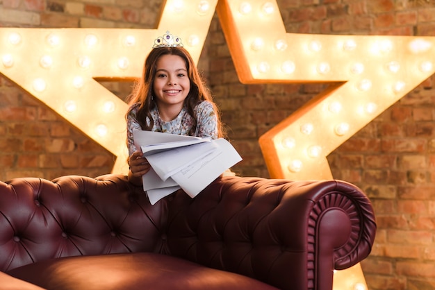 Free photo smiling girl standing behind the sofa against brick wall