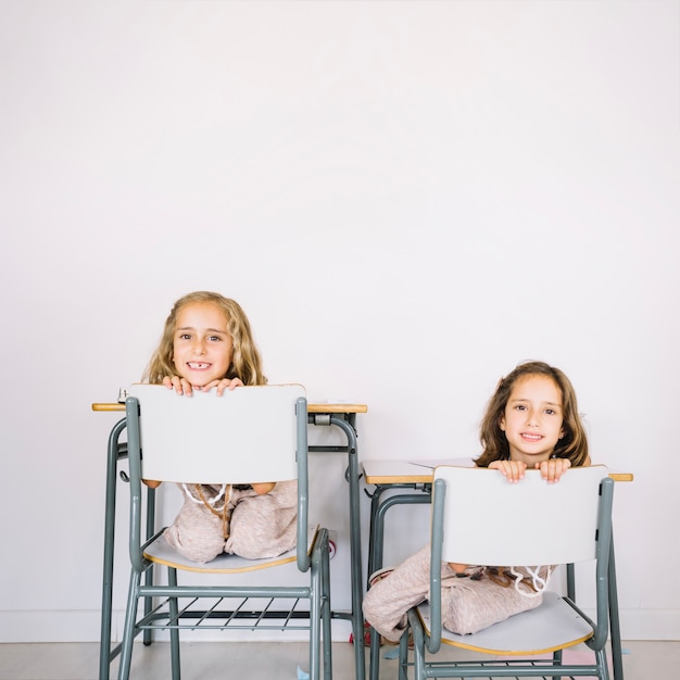 Free photo smiling girls peeking from behind chairs