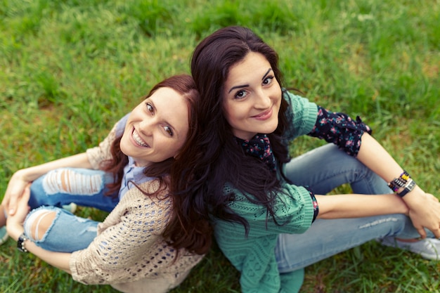 Smiling girls sitting back to back on grass