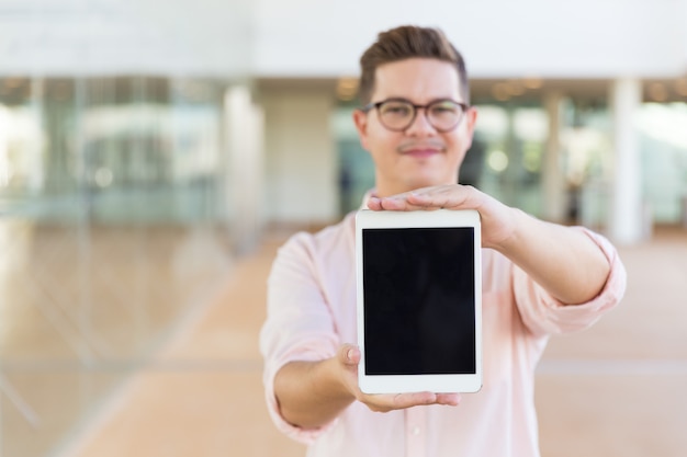 Smiling guy in glasses showing blank tablet screen