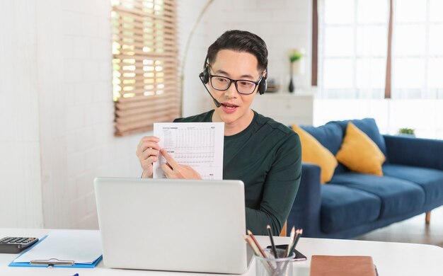 Smiling handsome asian businessman wear headphones working remotely from home. He is webinar video conference