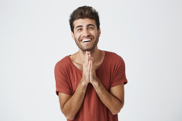 Smiling handsome italian unshaven guy holding palms pressed together in front of him feeling happy about birthday gift from wife.