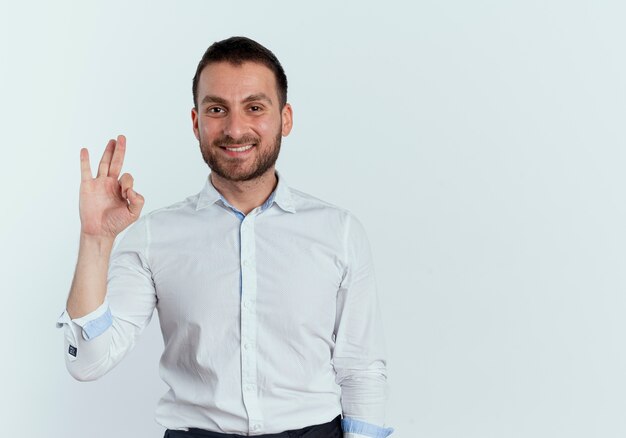 Smiling handsome man gestures ok hand sign isolated on white wall