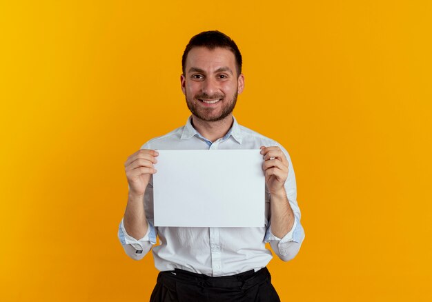 Smiling handsome man holds paper sheet isolated on orange wall