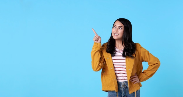 Smiling happy asian woman with her finger pointing isolated on light blue banner background with copy space.