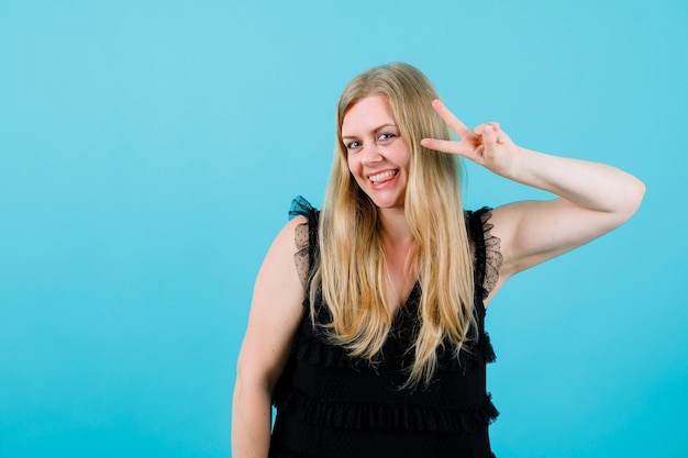 Smiling happy girl is showing two gesture on blue background