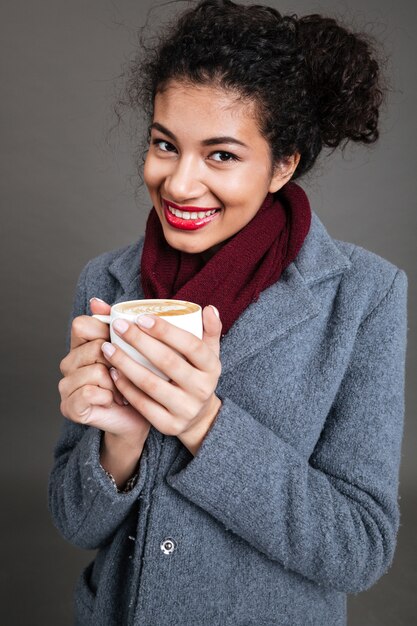 Smiling happy woman in coat holding cup of coffee