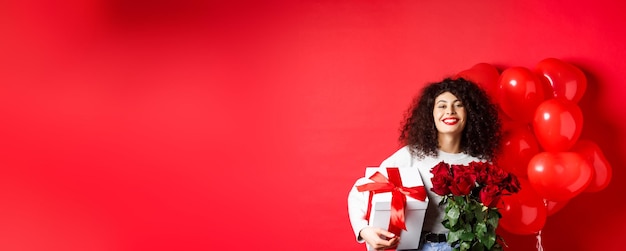 Free photo smiling happy woman holding box with gift and red roses from boyfriend celebrating valentines day st