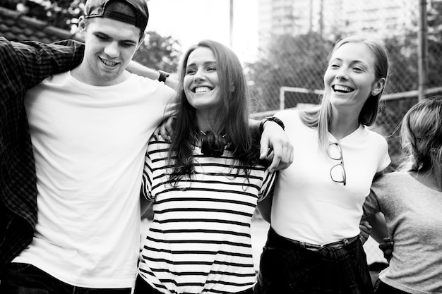 Smiling happy young adult friends arms around shoulder outdoors 