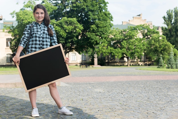 Free photo smiling highschool girl holding blackboard