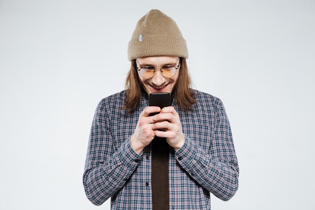 Smiling hipster in eyeglasses using smartphone