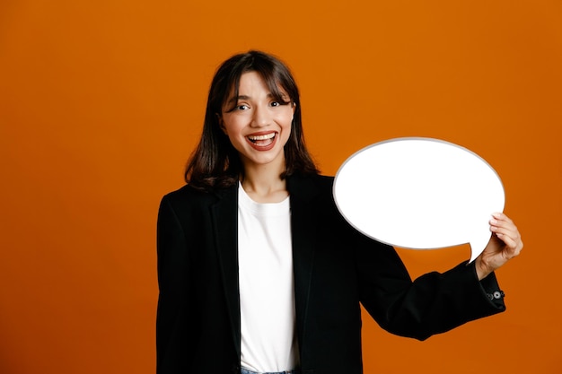 smiling holding speech bubble young beautiful female wearing black jacket isolated on orange background