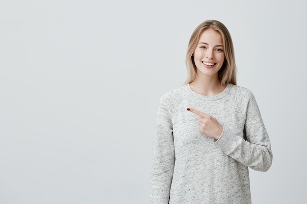 Smiling joyful woman pointing with finger at copyspace