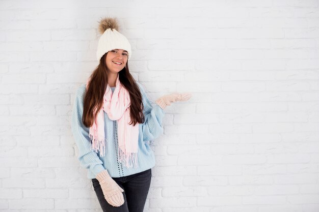 Smiling lady in mittens, bobble hat and scarf with opened hand 