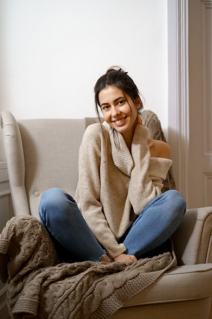 Free photo smiling lady in smart trendy wear is sitting on armchair. smiling, sitting in relaxing atmosphere indoors