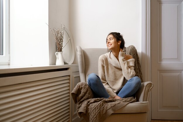 Smiling lady in smart trendy wear is sitting on armchair. Smiling, sitting in relaxing atmosphere indoors