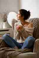 Free photo smiling lady in smart trendy wear is sitting on armchair with a cup of tea.