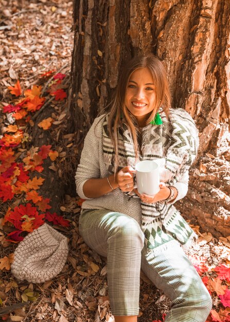 Smiling lady with beverage in autumn forest