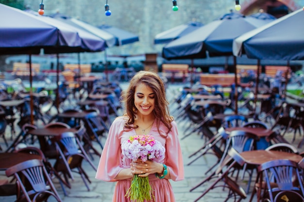 Free Photo smiling lady with flower bouquet stands among lonely tables in c