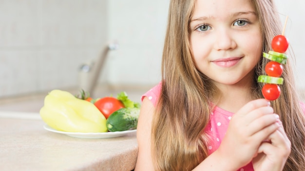 Free photo smiling little girl holding salad skewer in hand