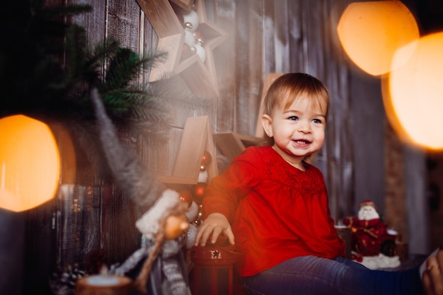 Free photo smiling little girl sits on the shelf between beautiful christmas decorations