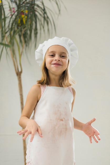 Smiling little girl wearing white apron and chef hat