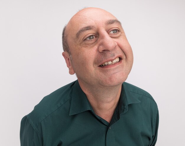 Smiling looking at side middle-aged man wearing green t-shirt isolated on white wall