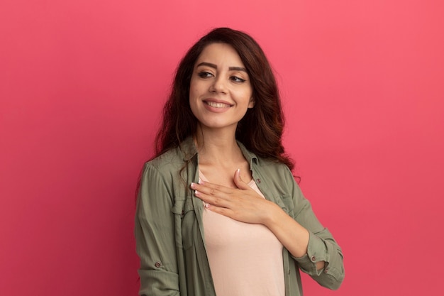 Free Photo smiling looking at side young beautiful girl wearing olive green t-shirt putting hand on chest isolated on pink wall