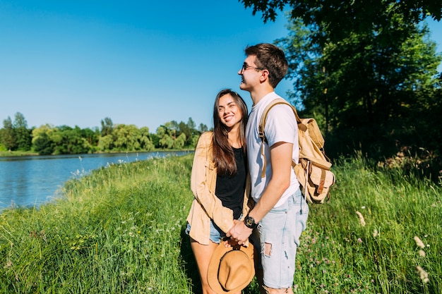 Free Photo smiling lovely young couple standing in green grass near the lake