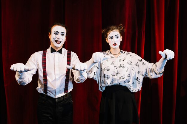 Smiling make mime and sad female mime showing their thumbs on stage