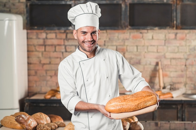 Smiling male baker holding baked bread on chopping board