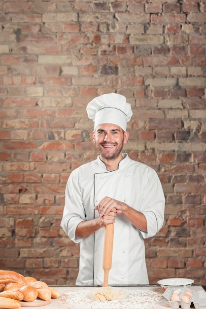 Free photo smiling male baker standing behind the table with dough and breads