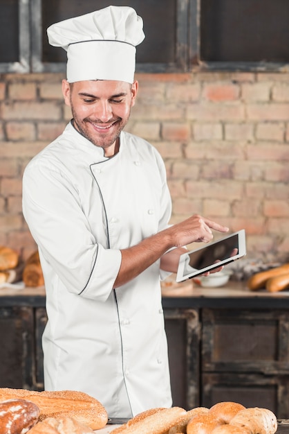 Smiling male baker using digital tablet looking at baked breads on table