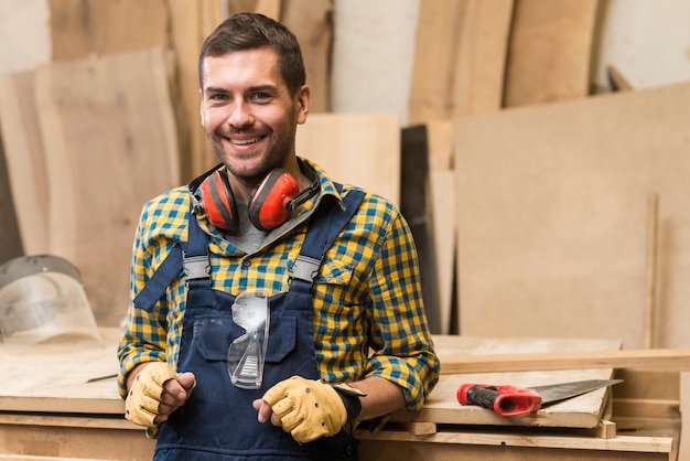 Free photo smiling male carpenter standing in front of workbench