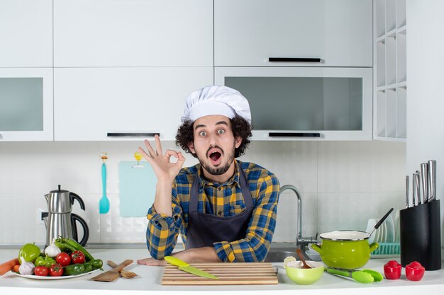 Smiling male chef with fresh vegetables making eyeglasses gesture in the white kitchen