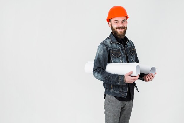 Smiling male engineer holding rolled up blueprint against white background