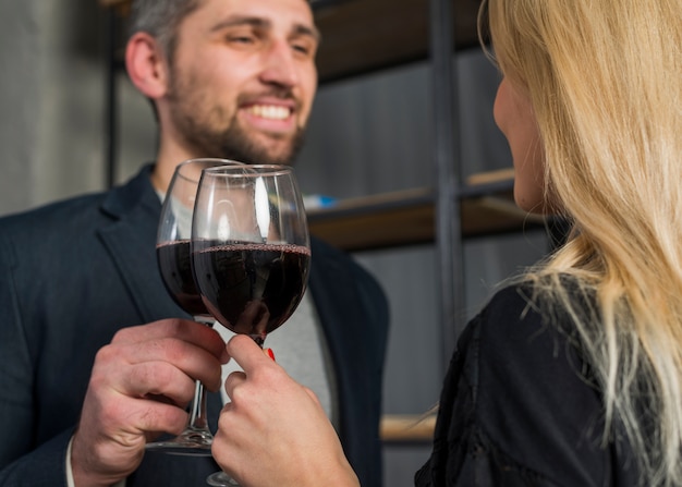 Smiling male and female clanging glasses of drink in room